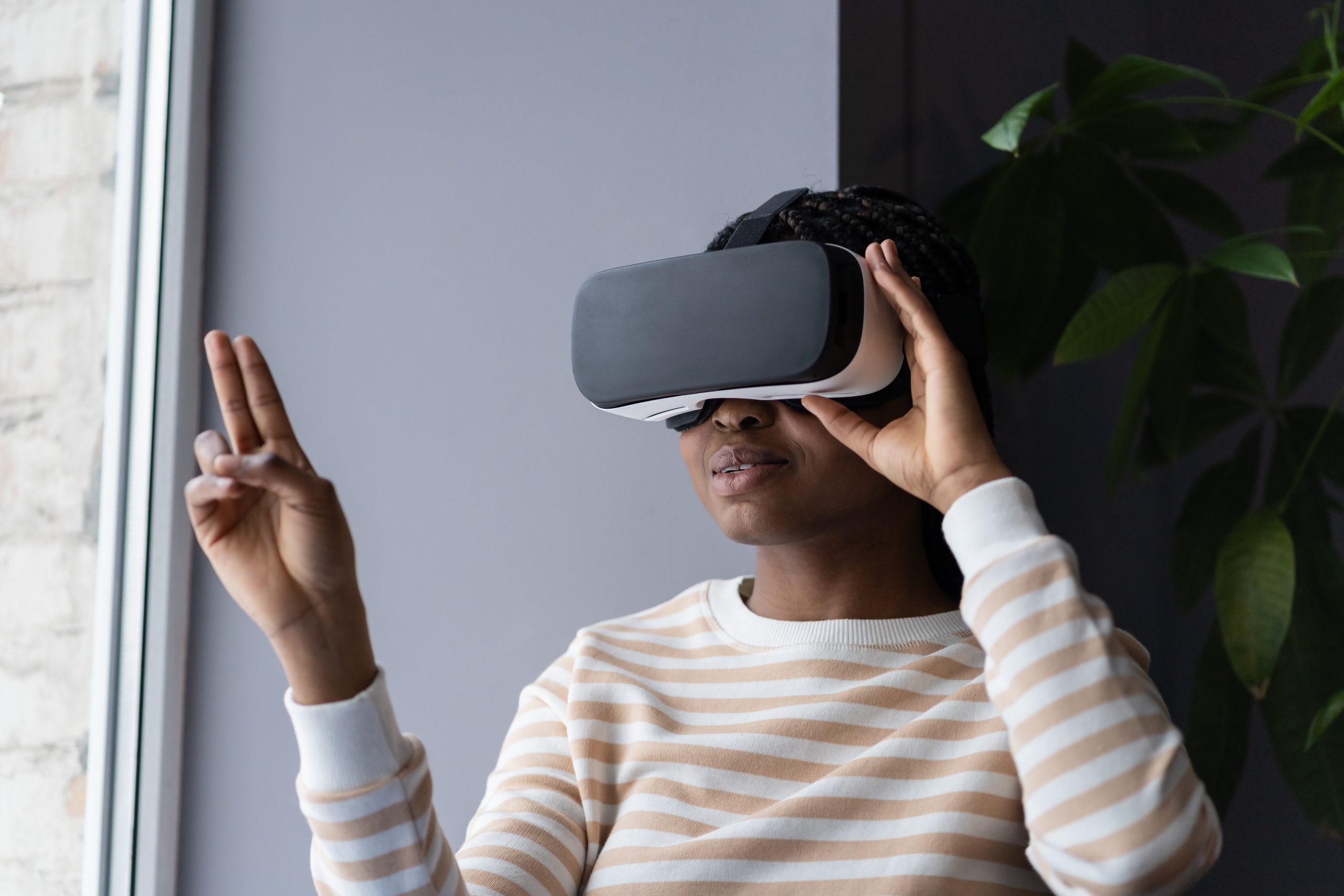 Black woman enjoying virtual reality shopping experience while sitting by window at home, african american female wearing VR helmet touching air with finger, testing modern hi-tech future gadget