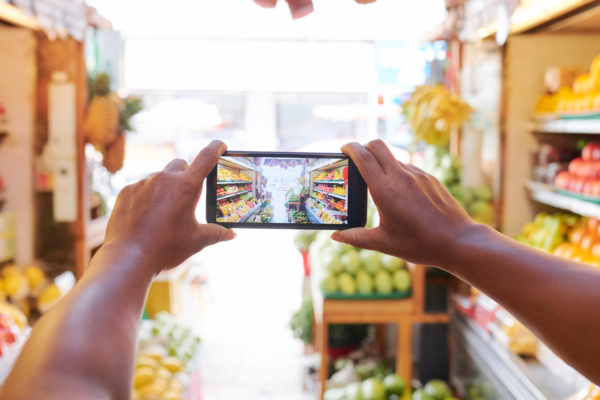 Close-up of female hands holding mobile phone and taking a photo of supermarket with fruits and vegetables department