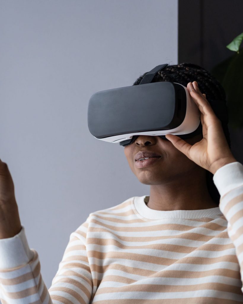Black woman enjoying virtual reality shopping experience while sitting by window at home, african american female wearing VR helmet touching air with finger, testing modern hi-tech future gadget