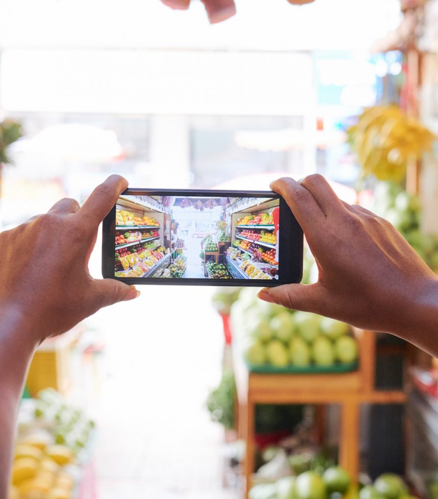 Close-up of female hands holding mobile phone and taking a photo of supermarket with fruits and vegetables department